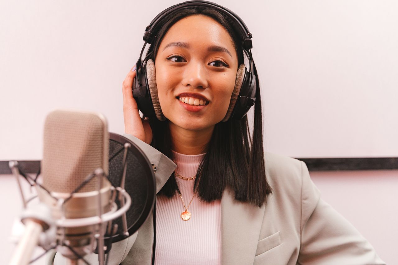 services-03 Smiling woman in a studio wearing headphones and speaking into a microphone for a podcast.